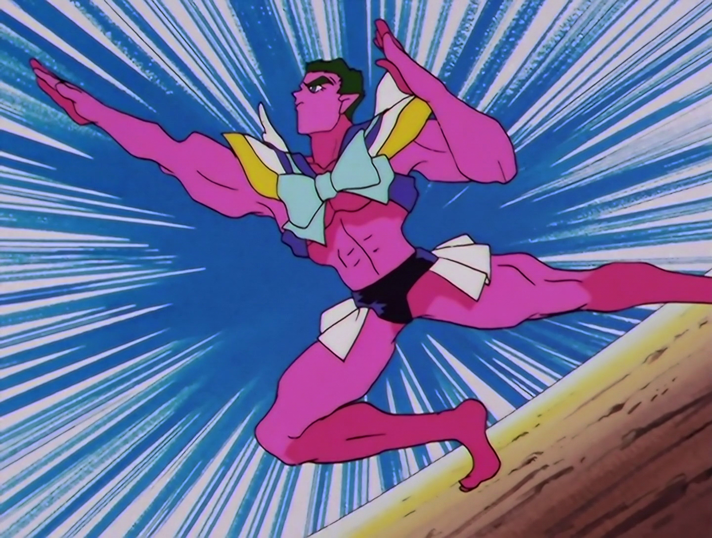 Sailor Guts, a Phage from Sailor Moon episode 174. He’s a big buff guy with short black hair and bright pink skin. He’s wearing a blue, white and yellow top with a large bow and angel wings on the mack, but it’s shaped so as to show off most of his midriff. He also has tiny black trunks, with white skirt-like sections on each side. He’s posing dramatically. What a king.